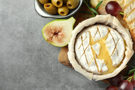Tasty baked brie cheese and products on gray table, flat lay. Space for text