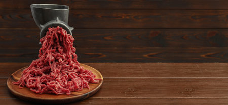 Mining beef with manual meat grinder on wooden table. Banner design with space for text