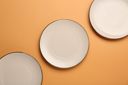 Beautiful beige ceramic plates on orange background, flat lay