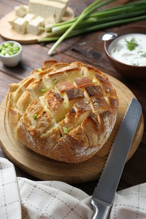 Freshly baked bread with tofu cheese, green onions, sauce and knife on wooden table