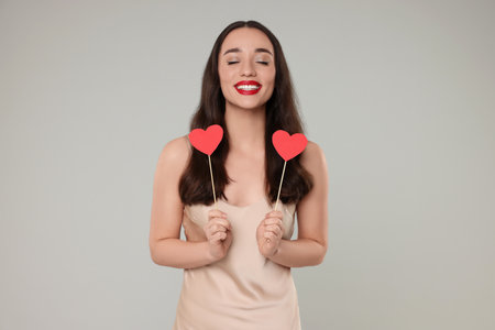 Beautiful young woman with paper hearts on gray backgroundの写真素材