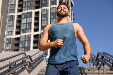 Happy man running down stairs outdoors on sunny day, low angle viewの写真素材