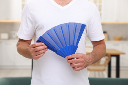 Man with blue hand fan in kitchen, closeupの写真素材