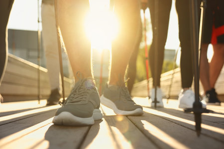 Group of people practicing Nordic walking with poles outdoors on sunny day, closeup
