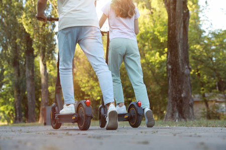 Couple riding modern electric kick scooters in park, back view