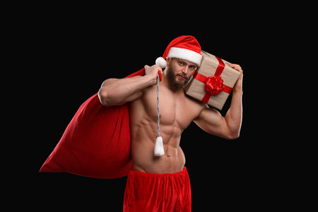 Attractive young man with muscular body holding bag and Christmas gift box on black backgroundの写真素材