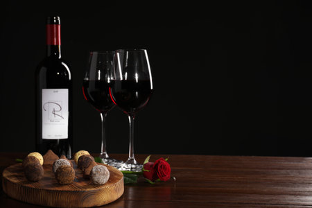 Red wine, chocolate truffles and rose flower on wooden table against dark background, space for textの写真素材