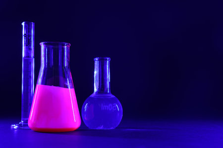 Laboratory glassware with luminous liquids on dark blue background, space for text