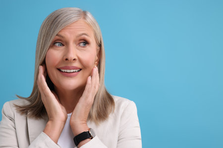 Portrait of happy middle aged woman on light blue background, space for text