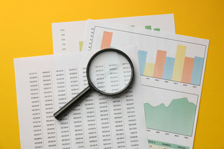 Accounting documents and magnifying glass on yellow background, top viewの写真素材