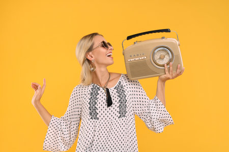 Portrait of happy hippie woman with retro radio receiver on yellow background