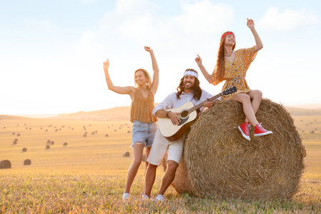 Beautiful hippie women listening to their friend playing guitar in field, space for text