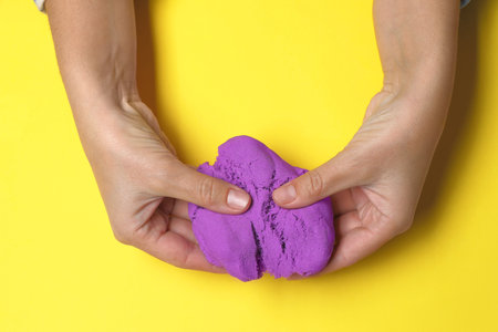 Woman playing with kinetic sand on yellow background, top viewの写真素材