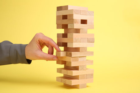Woman playing Jenga tower on yellow background, closeup