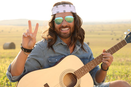 Happy hippie man with guitar showing peace sign in fieldの写真素材