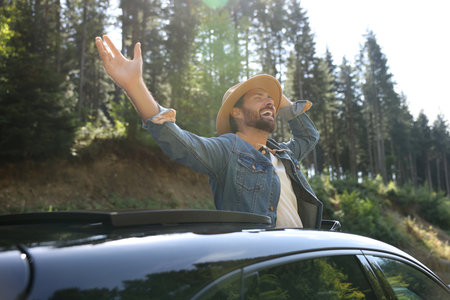 Enjoying trip. Happy man leaning out of car roof on sunny dayの写真素材
