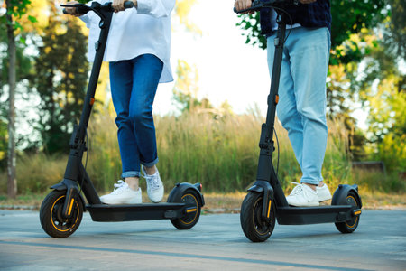 Couple riding modern electric kick scooters in park, closeupの写真素材