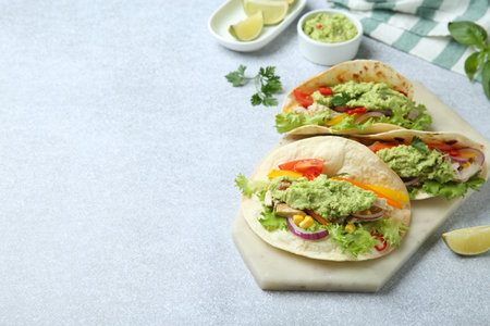 Delicious tacos with guacamole, meat and vegetables on light gray table, space for textの写真素材