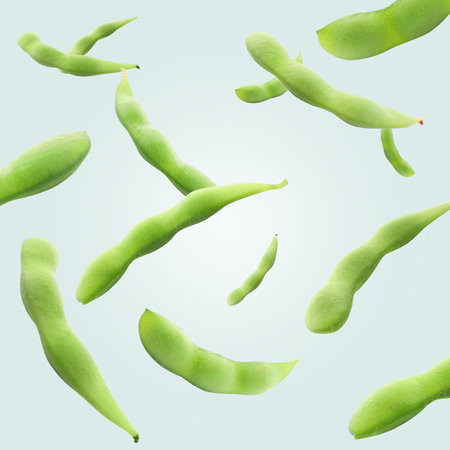 Green edamame pods falling on light aquamarine background