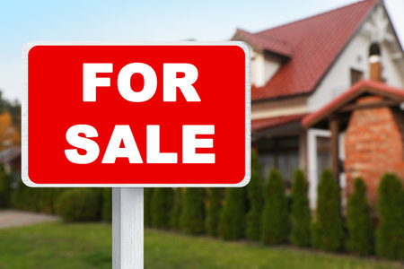 Sale sign near beautiful house outdoors. Red signboard with wordsの写真素材