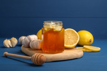 Honey with garlic in glass jar, lemons and dipper on blue wooden tableの写真素材