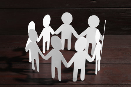 Teamwork concept. Paper figures of people holding hands on wooden table, closeupの写真素材