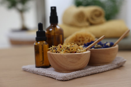 Bottles of essential oils, bowls with dry flowers and natural sponge on light wooden table, closeup. Spa therapyの写真素材