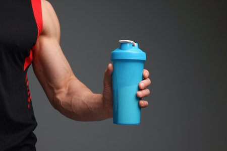 Young man with muscular body holding shaker of protein on gray background, closeup. Space for textの写真素材