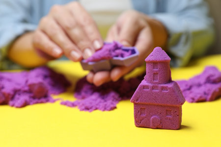Woman playing with kinetic sand at yellow table, selective focusの写真素材