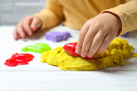 Little child playing with yellow kinetic sand at white wooden table, closeupの写真素材