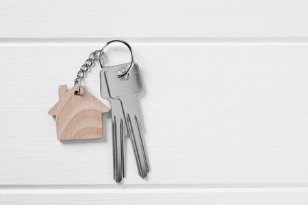 Key with keychain in shape of house on white wooden table, top view. Space for textの写真素材