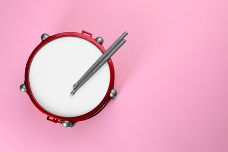 Children's drum with drumsticks on pink background, top view. Space for textの写真素材