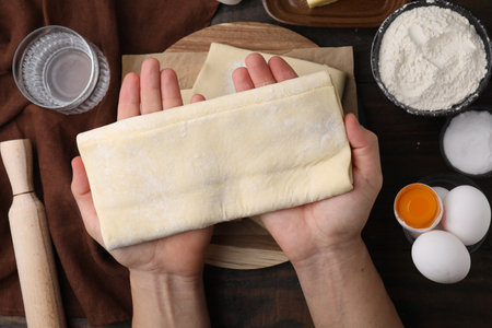 Man holding raw puff pastry dough at wooden table, top view