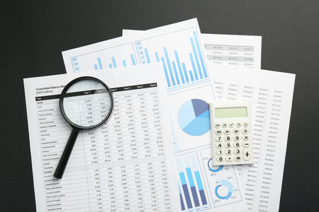 Accounting documents, calculator and magnifying glass on black table, top view