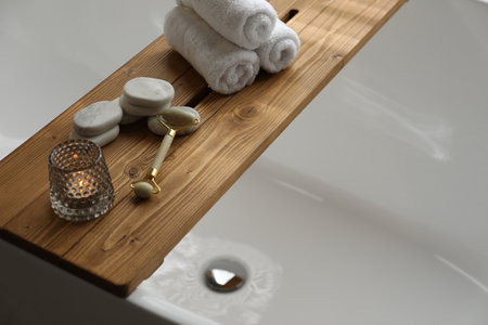 Wooden tray with spa products and burning candle on bath tubの写真素材