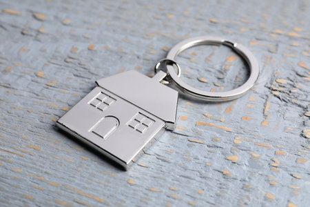 Metal keychain in shape of house on gray wooden table, closeup