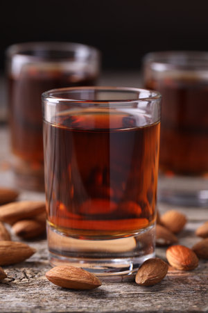 Shot glass with tasty amaretto liqueur and almonds on wooden table, closeup