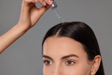 Beautiful woman applying hair serum on gray background, closeup. Cosmetic productの写真素材