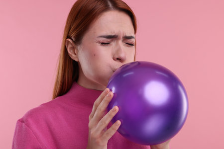 Woman inflating purple balloon on pink backgroundの写真素材