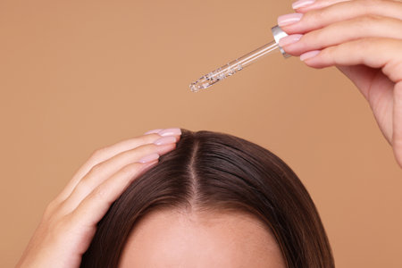 Woman applying serum onto hair on beige background, closeupの写真素材