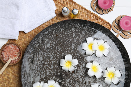 Bowl of water with plumeria flowers and different spa supplies on table, top viewの写真素材