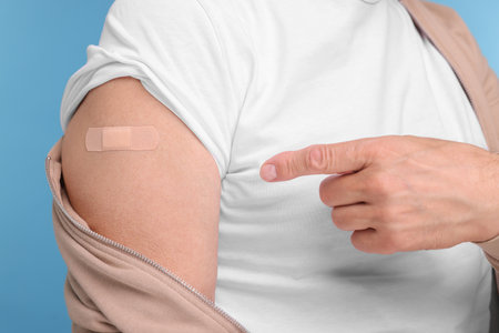 Man pointing at adhesive bandage after vaccination on light blue background, closeupの写真素材