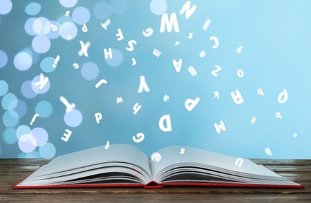 Letters flying out from open book on wooden table, bokeh effectの写真素材