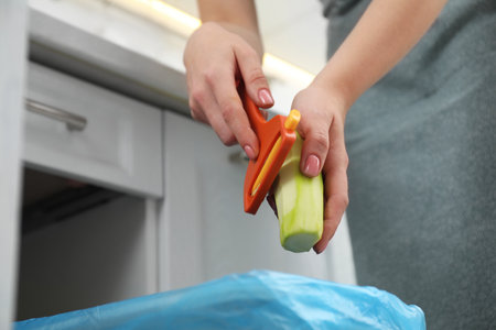 Woman peeling fresh zucchini above garbage bin indoors, closeupの写真素材