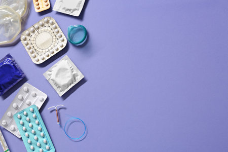 Contraceptive pills, condoms and intrauterine device on violet background, flat lay with space for text. Different birth control methodsの写真素材
