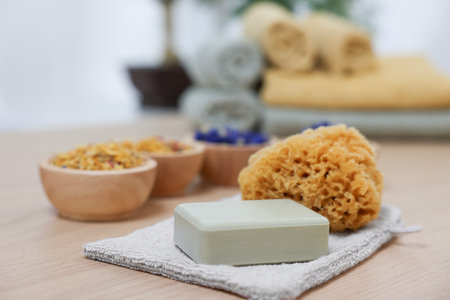 Soap bar, natural sponge and bowls of dry flowers on light wooden table. Spa therapy