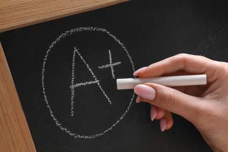 School grade. Teacher writing letter A and plus symbol with chalk on blackboard, closeupの写真素材
