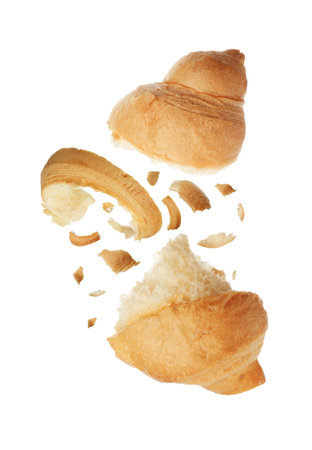 Pieces of delicious fresh croissant falling on white background