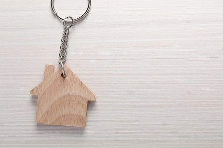 One keychain in shape of house on light wooden table, top view. Space for text