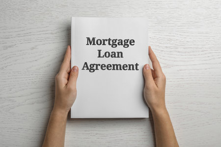 Woman holding mortgage loan agreement on white wooden table, top viewの写真素材
